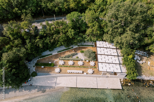 Festive tables stand on wooden flooring in a green garden by the sea. Drone
