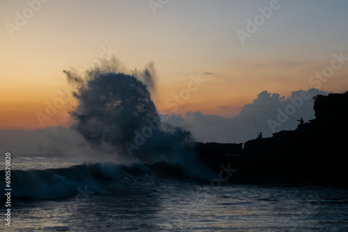 Sunset at Balinese coast, Indonesia, silhouette of fishermen in front of giant waves