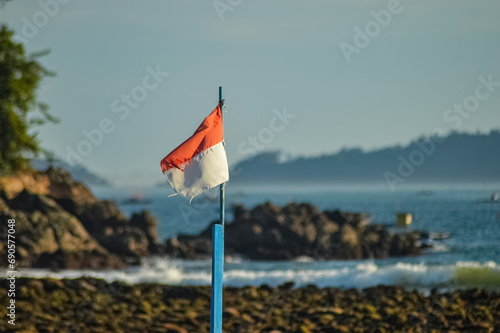 The Indonesian flag fluttering in the wind against the backdrop of a coral rocky beach that looks blurry photo