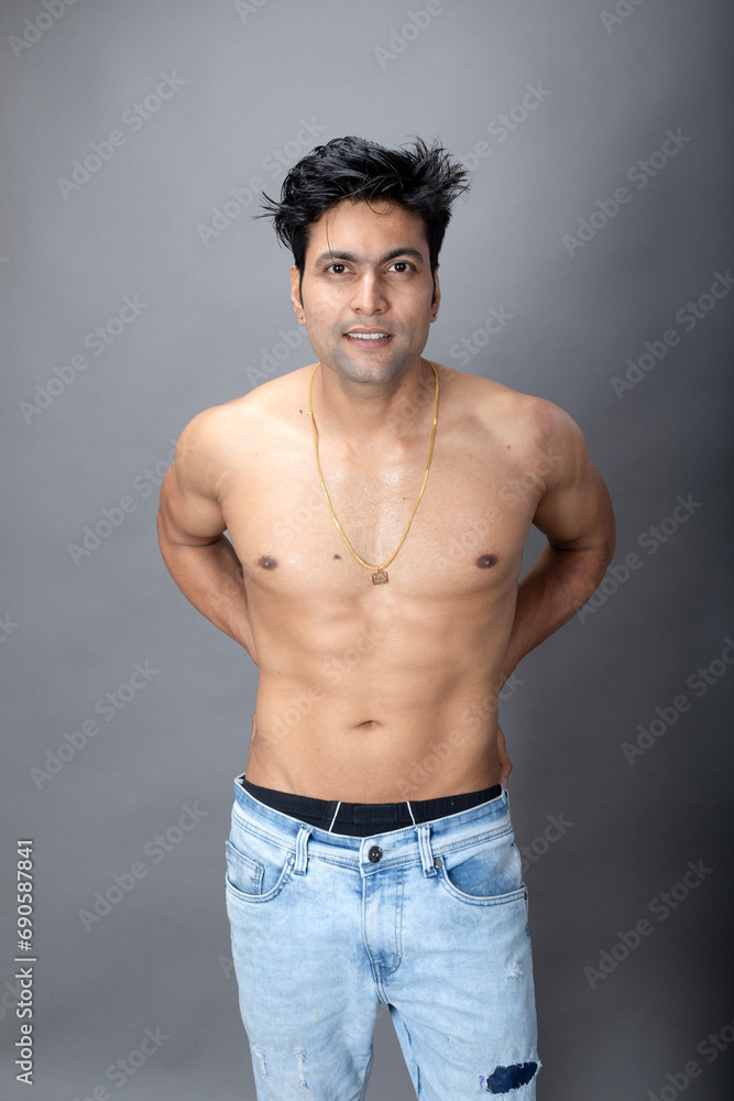 Portrait of a shirtless young man. Healthy muscular man with black hair, posing with bare upper body, hands in pocket on grey background. Portrait of a shirtless young man. Healthy muscular man with black hair, posing with bare upper body, hands in pocket on grey background.