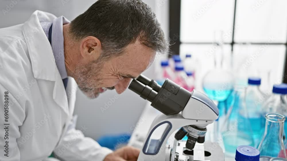 Smiling middle age man with grey hair, joyfully embracing science in his laboratory, using microscope Smiling middle age man with grey hair, joyfully embracing science in his laboratory, using microscope