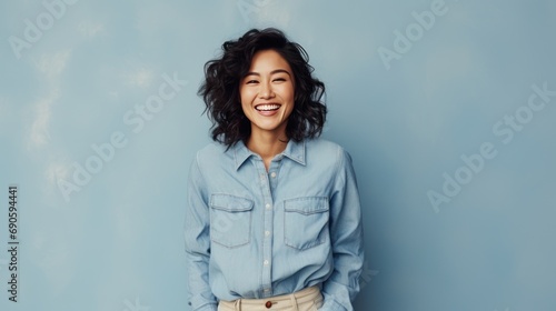 Beautiful attractive Asian female with casual jean smile cheerful standing against plain background peach color, young happy student or worker woman soft skin charming face with long curly hairstyle