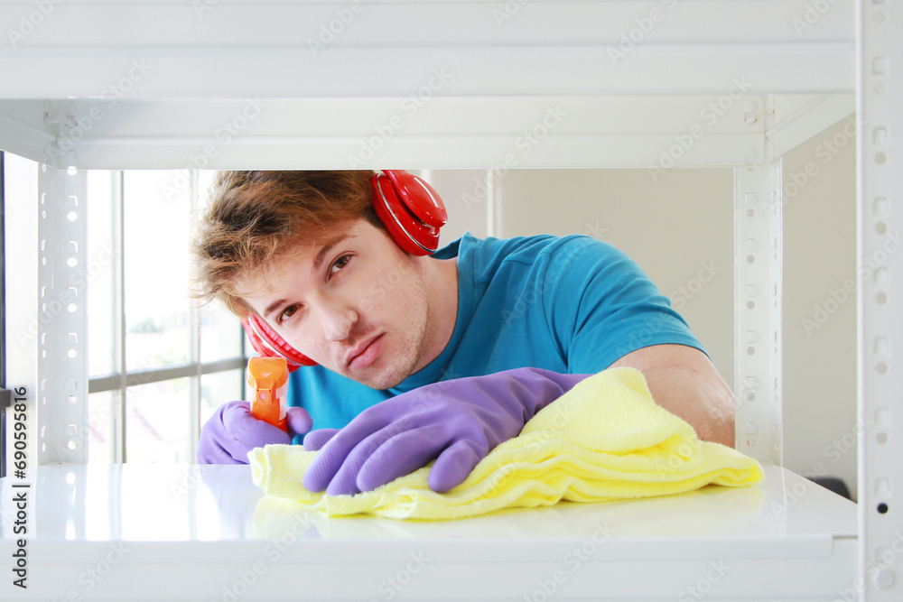 Young Caucasian male Wearing violet rubber gloves is holding Cleanser bottle and sponge. He is cleaning and wiping on white Shelf for housework.Lifestyle of Family man on Holiday Concept Young Caucasian male Wearing violet rubber gloves is holding Cleanser bottle and sponge. He is cleaning and wiping on white Shelf for housework.Lifestyle of Family man on Holiday Concept