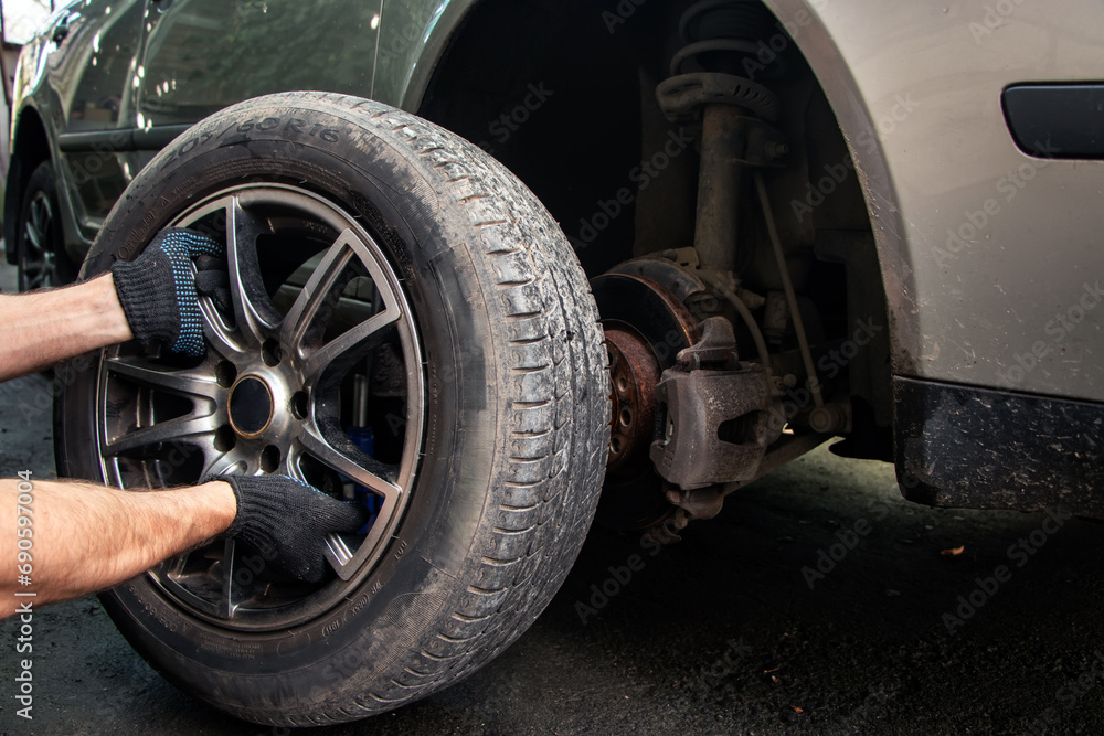 Car repairs. Replacing wheels. Seasonal tire replacement. The master removes the wheel with both hands with the key.