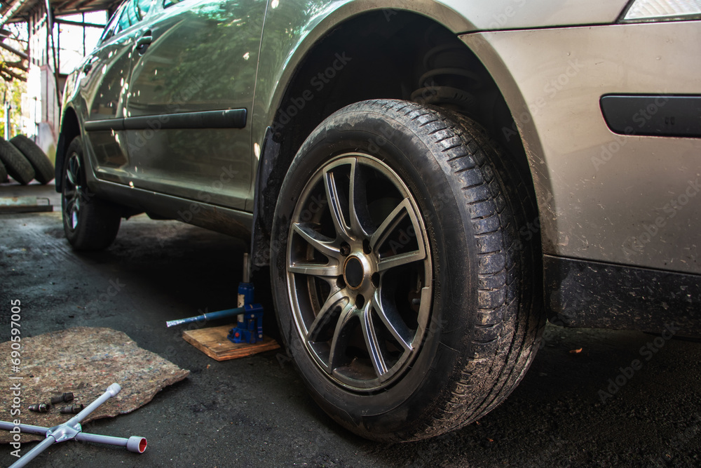 Car lifted by scissor jack without wheel outdoors, closeup. Tire puncture Car lifted by scissor jack without wheel outdoors, closeup. Tire puncture