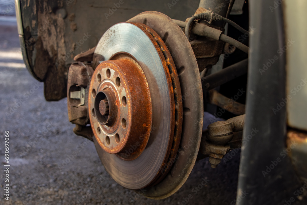 Old front brake disc with caliper and brake pads in the car, on a car lift in a workshop, close-up of a brake caliper. Old front brake disc with caliper and brake pads in the car, on a car lift in a workshop, close-up of a brake caliper.