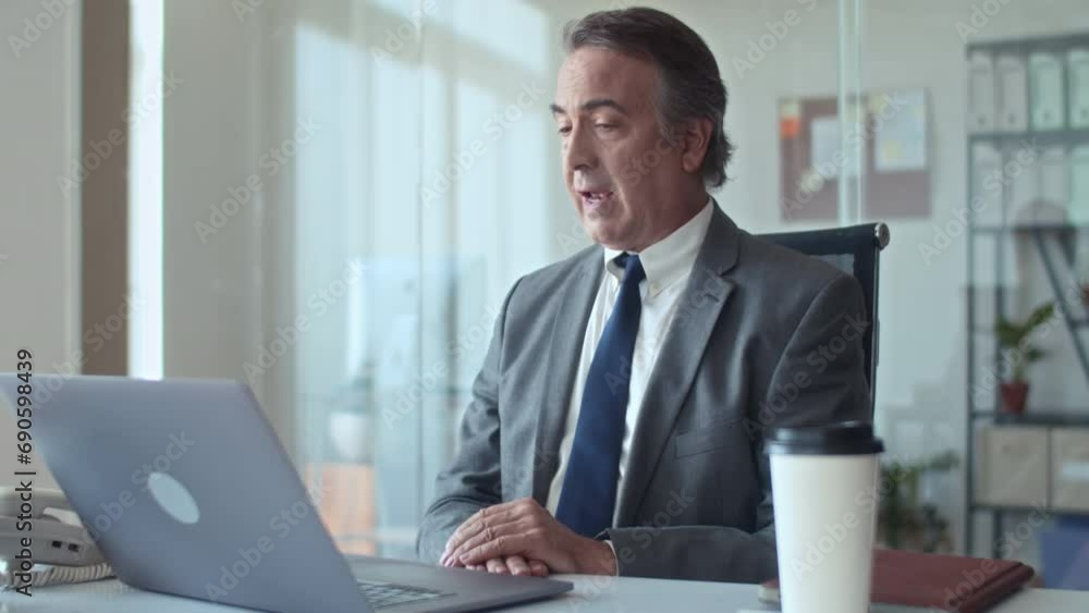 Medium shot of senior businessman making video call to his colleague while sitting in front of laptop in office Medium shot of senior businessman making video call to his colleague while sitting in front of laptop in office