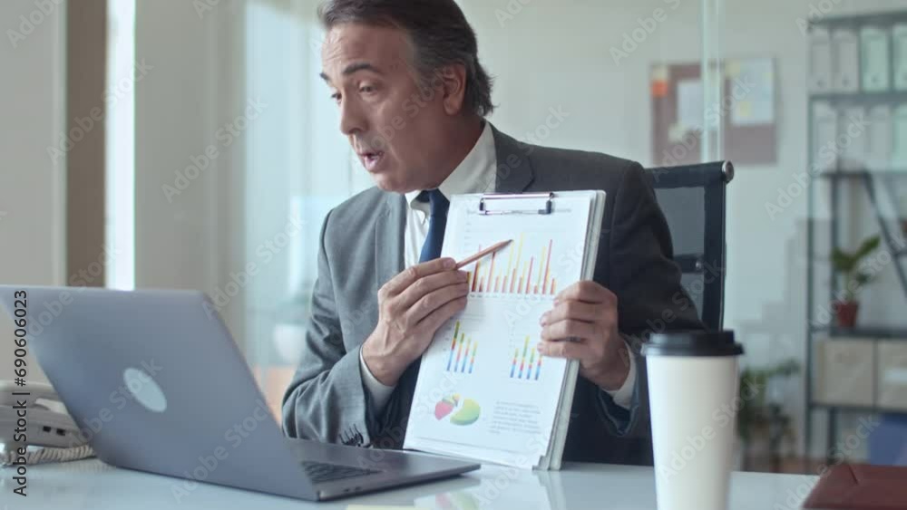 Medium shot of mature sales manager showing business chart with data to his interlocutor during video call using laptop Medium shot of mature sales manager showing business chart with data to his interlocutor during video call using laptop