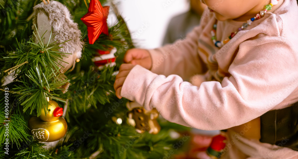 Little girl placing ornaments on the Christmas tree with golden glittering lights.