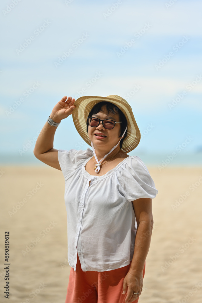 Vertical Portrait image of Middle aged Asian woman in hat with summer beach background Vertical Portrait image of Middle aged Asian woman in hat with summer beach background