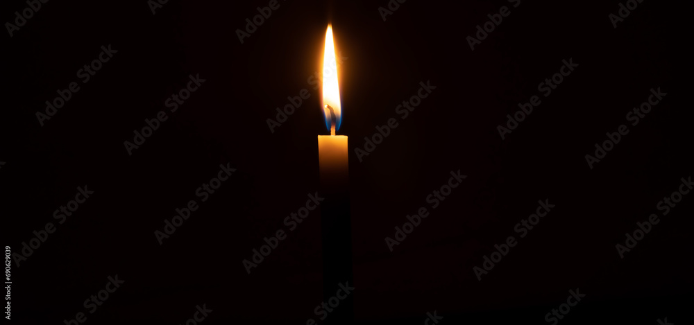Single burning candle flame or light glowing on a small yellow candle on black or dark background on table in church for Christmas, funeral or memorial service with copy space. Single burning candle flame or light glowing on a small yellow candle on black or dark background on table in church for Christmas, funeral or memorial service with copy space.