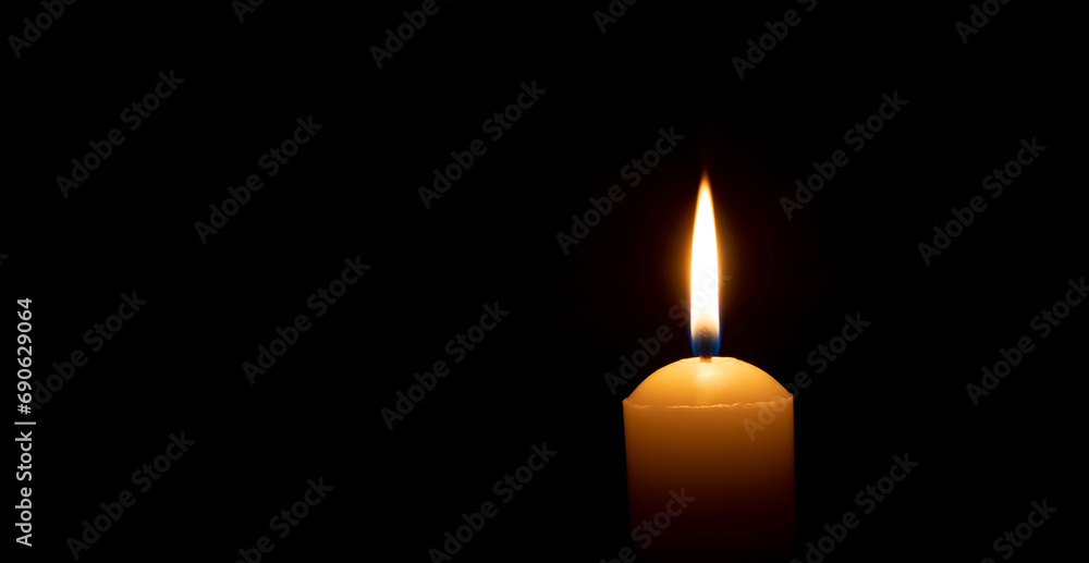 Single burning candle flame or light glowing on a big yellow candle on black or dark background on table in church for Christmas, funeral or memorial service with copy space Single burning candle flame or light glowing on a big yellow candle on black or dark background on table in church for Christmas, funeral or memorial service with copy space