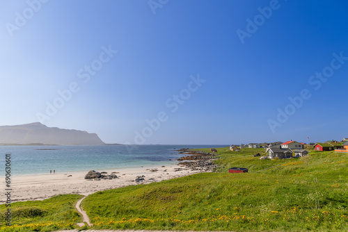 A couple makes their way to the shimmering azure waters for a swim at the white-sanded Rambergstranda beach on Flakstadoya island, Lofoten. Norway