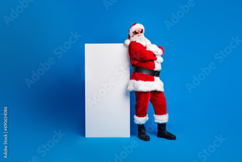 Full length photo of elderly retired man folded arms lean on ad dressed stylish santa claus costume coat isolated on blue color background