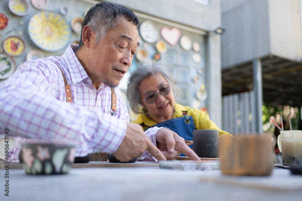 In the pottery workshop, an Asian retired couple is engaged in pottery making and clay painting activities. In the pottery workshop, an Asian retired couple is engaged in pottery making and clay painting activities.