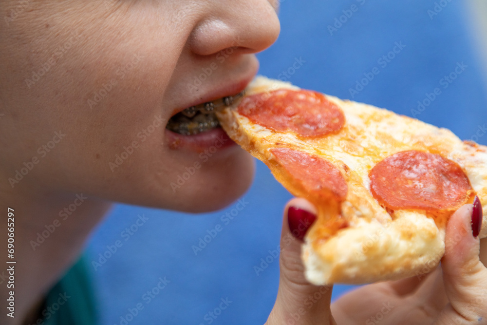 Closeup of woman with dental braces eating slice of pizza Closeup of woman with dental braces eating slice of pizza