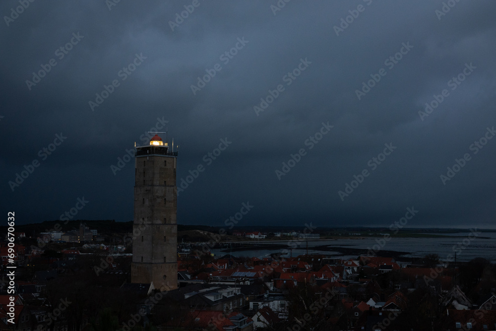 Lighthouse Brandaris on the Dutch island Terschelling by night under a cloudy sky, lights in the village below