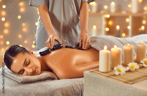 Фотография Serene attractive brunette woman getting hot stone massage in spa salon