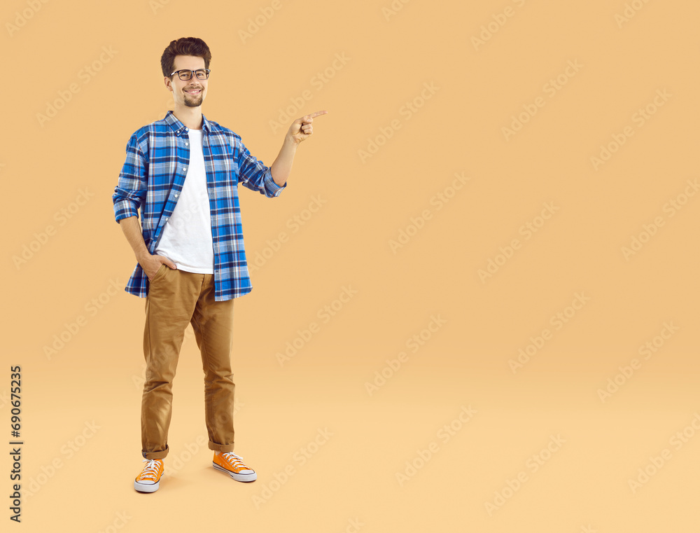 Full-size photo of happy, well-groomed, young man in glasses with beard and mustache, dressed in white T-shirt and plaid shirt, smiling and pointing his finger to the side at empty isolated copy space Full-size photo of happy, well-groomed, young man in glasses with beard and mustache, dressed in white T-shirt and plaid shirt, smiling and pointing his finger to the side at empty isolated copy space