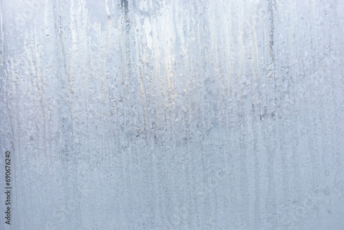 Winter window with frozen vertical water stripes. Frosty patterns on winter iced white window glass