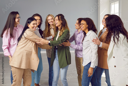 Portrait of a group of happy cheerfull young diverse women friends coworkers and company employees hugging and laughing on grey background. Diversity, team work and friendship concept. photo