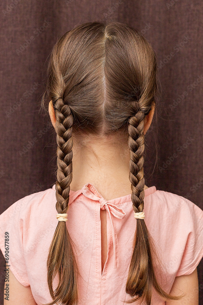 Close-up of a girl's hairstyle with a lush braid, view from the back. Hair styling is done with hairpins and an elastic band. Only the back of the head with a haircut