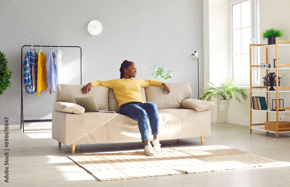 African american relaxed woman sitting on comfortable couch in the living room at modern home and smiling. Young calm peaceful girl enjoying quiet time alone in the room resting and dreaming. African american relaxed woman sitting on comfortable couch in the living room at modern home and smiling. Young calm peaceful girl enjoying quiet time alone in the room resting and dreaming.