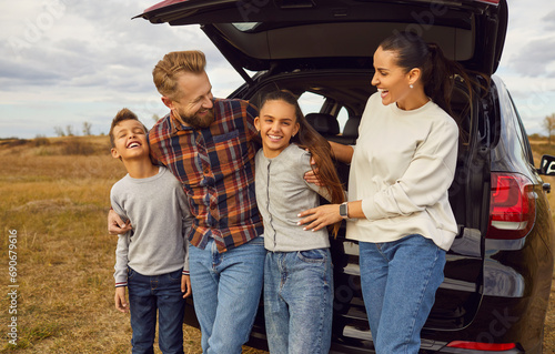 Portrait of happy smiling family of four with two kids boy and girl having fun and hugging standing near the trunk of their car enjoying weekend in nature. Vacation and road trip concept © Studio Romantic