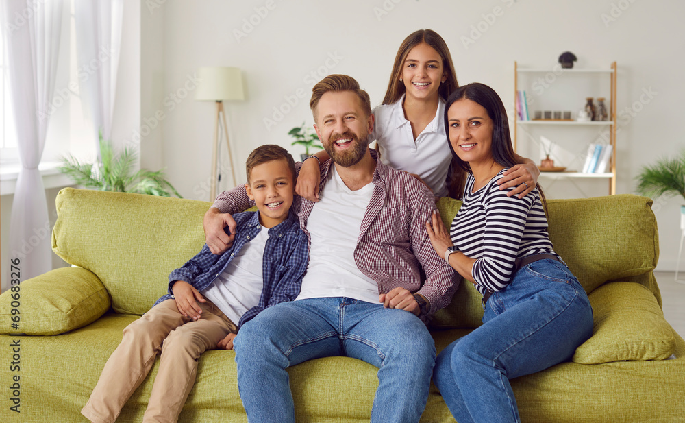 Parents and children spending time together. Happy family of four on sofa at home. Portrait of cheerful, smiling mother, father, son and daughter sitting on green couch in cozy living room interior
