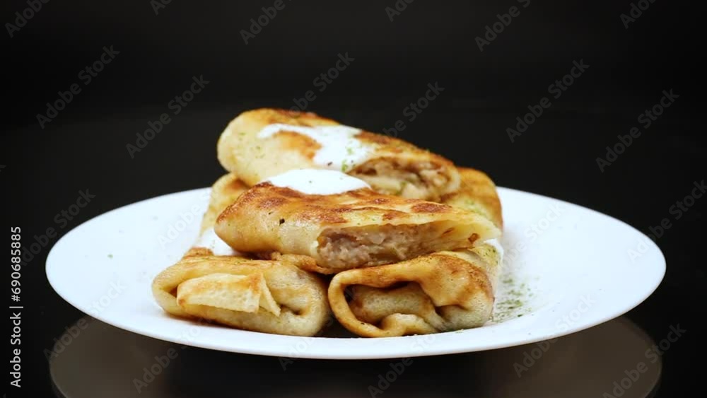 Thin fried pancakes with meat filling in a plate with sour cream and spices. Thin fried pancakes with meat filling in a plate with sour cream and spices.