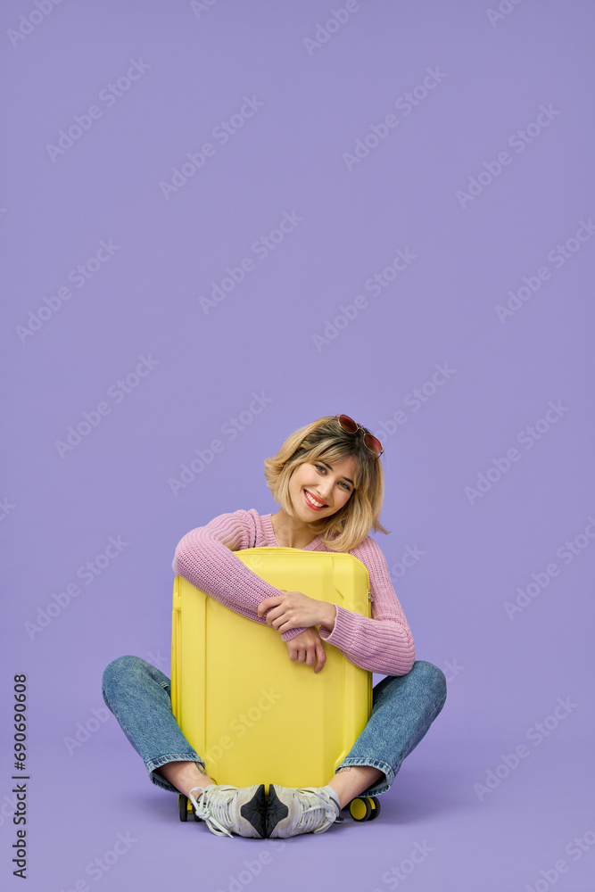 Happy young woman traveler, smiling stylish girl tourist hugging yellow luggage travel suitcase ready for summer journey vacation trip looking at camera sitting on floor isolated on purple background. Happy young woman traveler, smiling stylish girl tourist hugging yellow luggage travel suitcase ready for summer journey vacation trip looking at camera sitting on floor isolated on purple background.