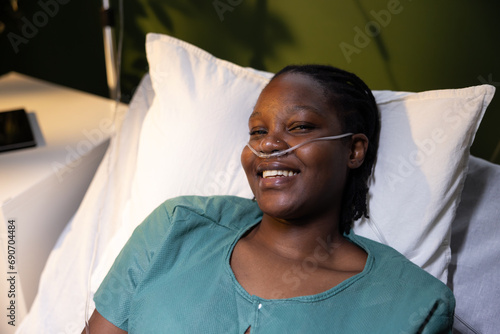 African woman lying in the hospital bed, wearing an oxygen tube, smiles at the camera.