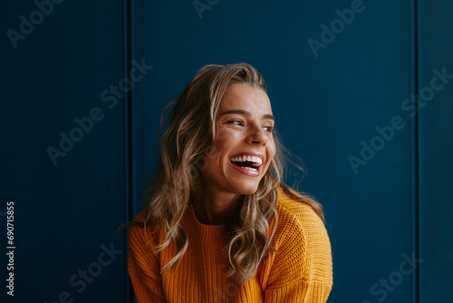 Happy young blond hair woman in yellow sweater looking away while standing on blue background photo