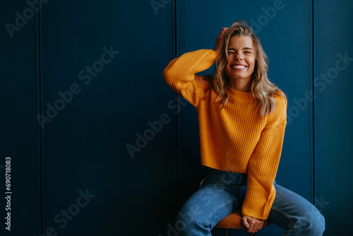 Playful young blond hair woman holding hand in hair and winking while sitting on blue background