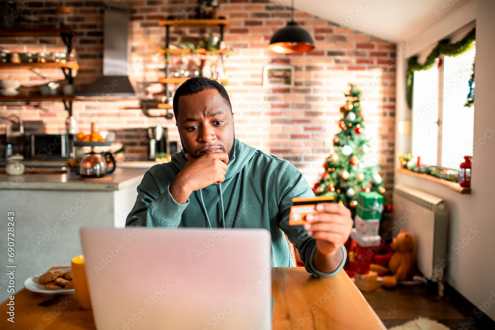Young man using credit card thinking at home Young man using credit card thinking at home