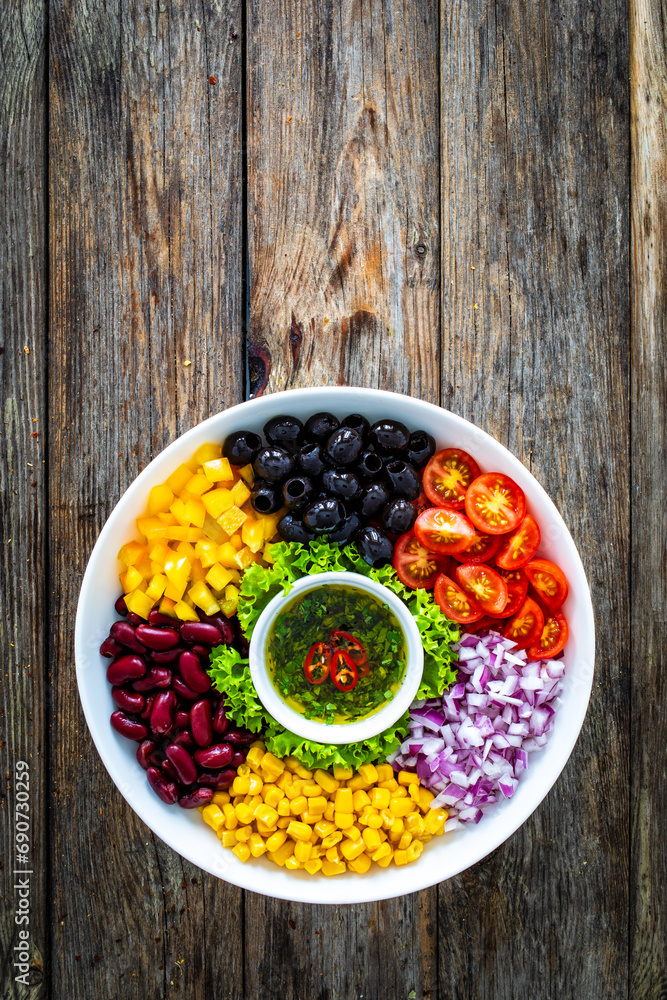 Mexican style salad - red beans, black olives, corn, yellow pepper, onion and tomatoes on wooden table Mexican style salad - red beans, black olives, corn, yellow pepper, onion and tomatoes on wooden table