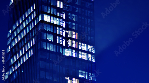 Fragment of the glass facade of a modern corporate building at night. Big glowing windows in modern office buildings at night, in rows of windows light shines. Blue graphic filter.