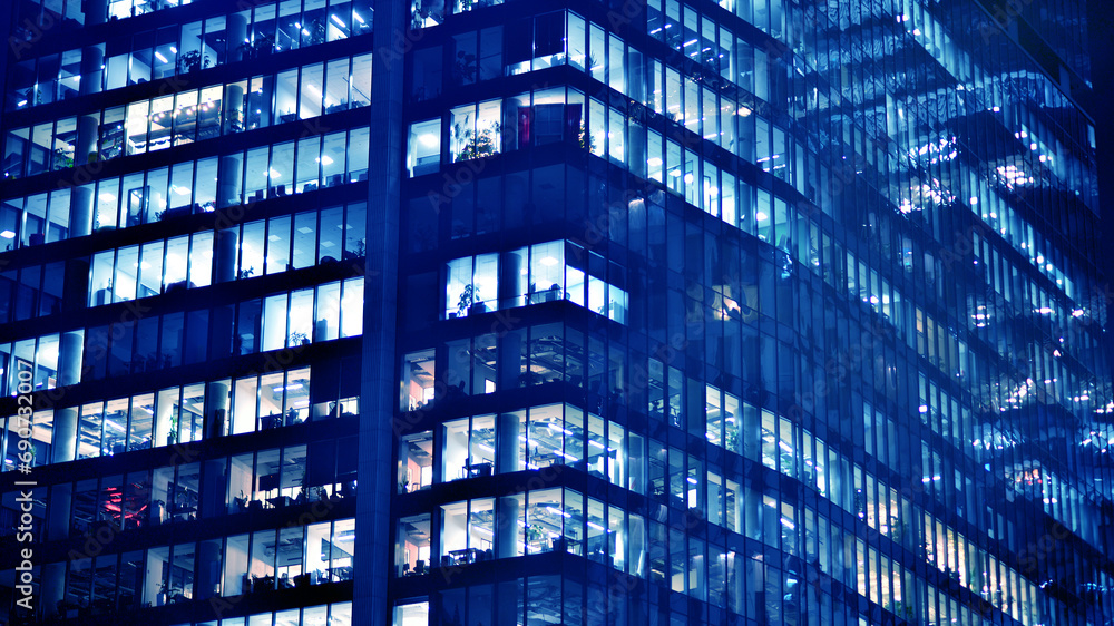 Fragment of the glass facade of a modern corporate building at night. Big glowing windows in modern office buildings at night, in rows of windows light shines. Blue graphic filter. Fragment of the glass facade of a modern corporate building at night. Big glowing windows in modern office buildings at night, in rows of windows light shines. Blue graphic filter.
