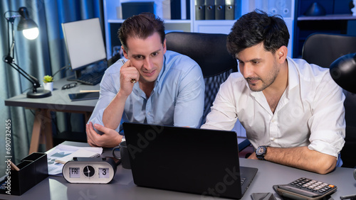 Business partners focusing on laptop, working together with good relation at night time in modern office, analyzing on creative project at blue neon decorative room. Concept of brainstorm. Sellable.