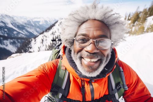 Happy mature african american hiker man taking selfie portrait on top of a snowy mountain