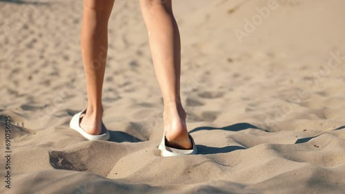 Close-up of young woman's feet walking in white flip-flops or slippers on white hot sand on hot sunny day. Camera follows woman, movement. photo