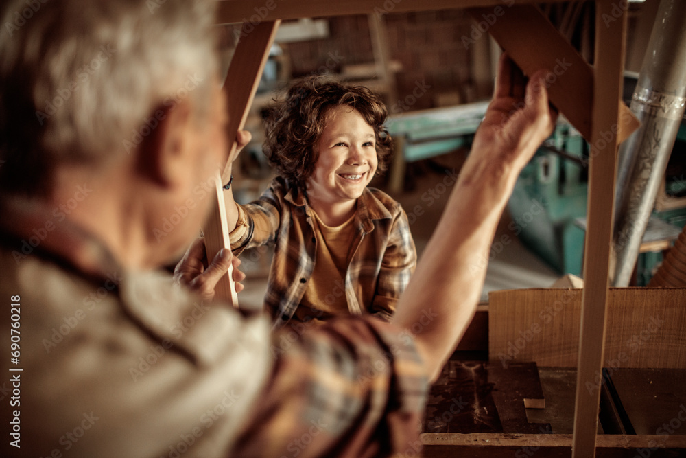 Elderly carpenter making wood frame with little boy in workshop Elderly carpenter making wood frame with little boy in workshop