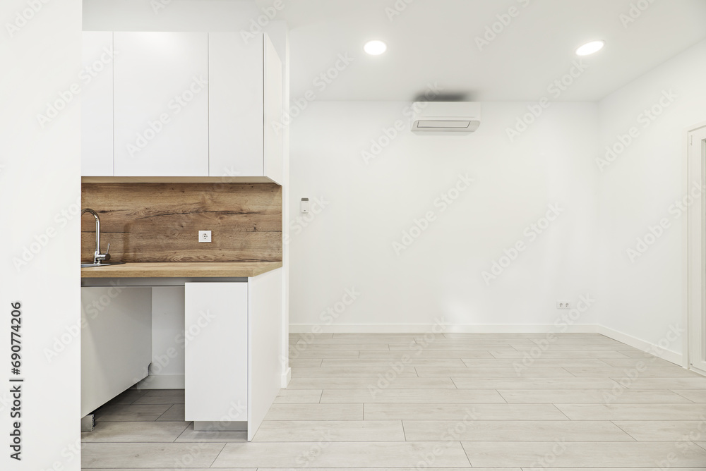 Image of a newly installed small kitchen with white furniture with backsplash and countertop of the same material in a loft-style apartment - obrazy, fototapety, plakaty 