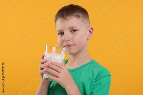 Cute boy with glass of fresh milk on orange background