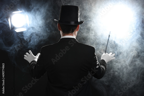 Magician with wand in smoke on stage, back view