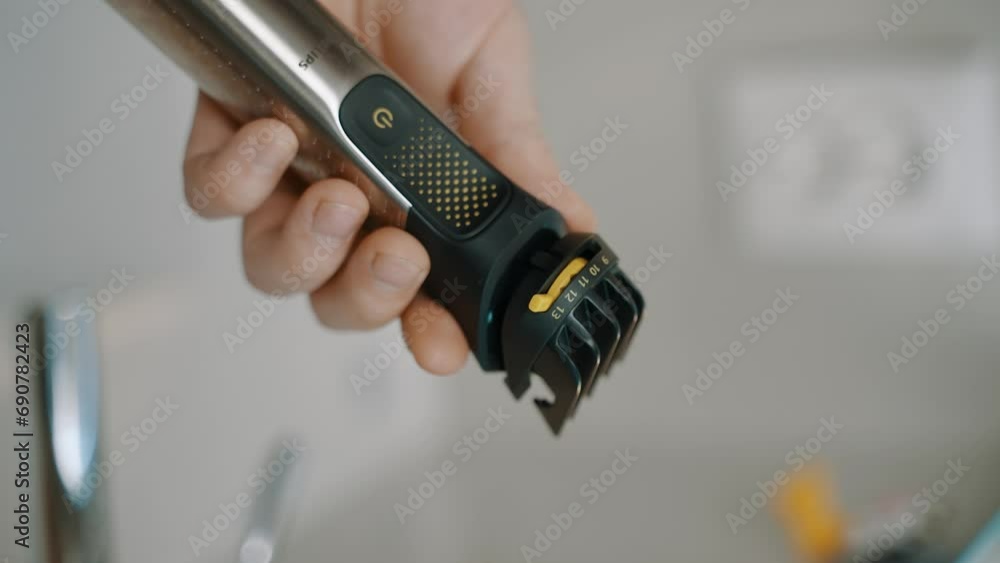 Hand holding an electric hair clipper with an adjustable guard, set against a blurred background, suggesting a grooming or haircutting scenario. Hand holding an electric hair clipper with an adjustable guard, set against a blurred background, suggesting a grooming or haircutting scenario.