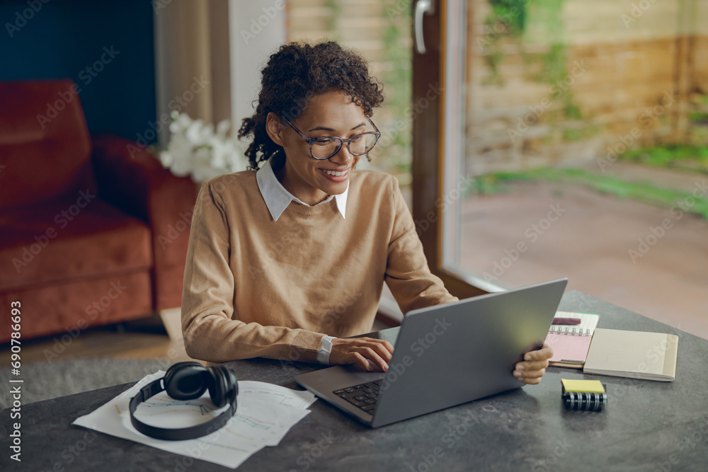 Smiling female manager working remotely on laptop from home while sitting at living room