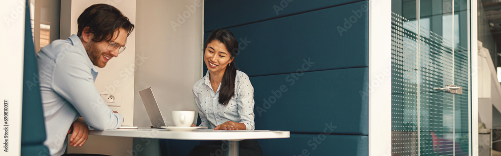 Two coworkers working together on project while using laptop in office meeting room