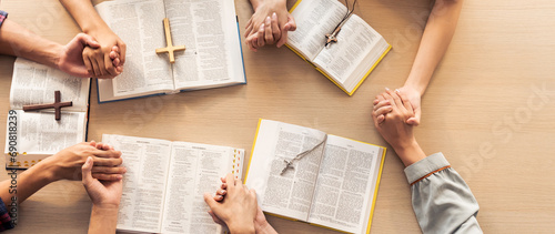 Cropped image of group of people praying together while holding hand on holy bible book at wooden church. Concept of hope, religion, faith, christianity and god blessing. Top view. Burgeoning. photo