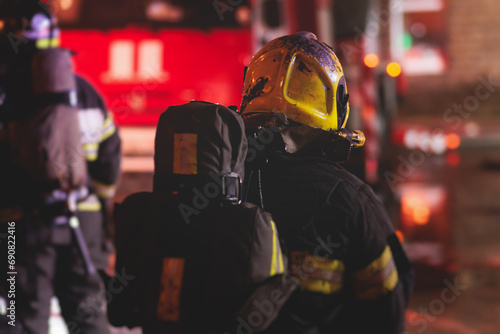 Group of fire men in protective uniform during fire fighting operation in the night city streets, firefighters brigade with the fire engine truck vehicle, emergency and rescue service photo